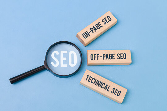 Three wooden blocks labeled "On-Page SEO," "Off-Page SEO," "Technical SEO" beside a magnifying glass focusing the word &ldquo;SEO,&rdquo; on blue background, representing  the three main pillars of SEO