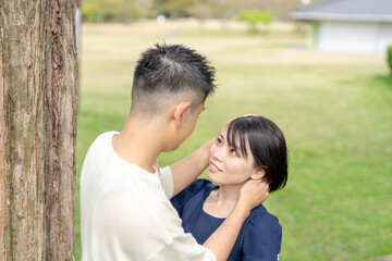 Obraz premium In the spring scene in May, we see an unmanned park in Jokojicho, Gokojicho, Eri Prefecture. Japanese couples in their early 20s spend time together.They stare at each other by a large tree.
