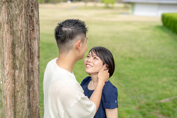 Fototapeta premium In the spring scene in May, we see an unmanned park in Jokojicho, Gokojicho, Eri Prefecture. Japanese couples in their early 20s spend time together.They stare at each other by a large tree.