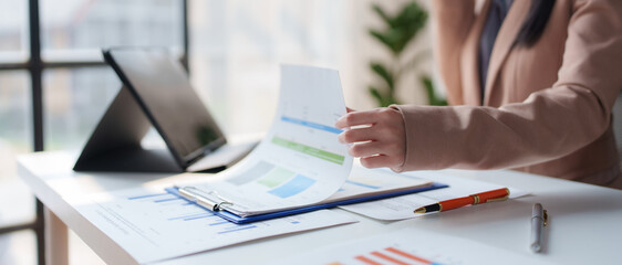 Businesswoman reviewing financial reports and charts using a digital tablet, assessing performance,...