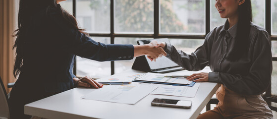 Two businesswomen shaking hands after reaching an agreement during a productive meeting,...