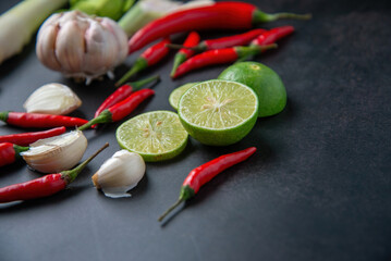 Fresh limes, garlic, and red chili peppers on dark surface, cooking ingredients