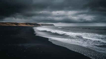 Obraz premium Dramatic black sand beach under ominous, cloudy sky. Crashing waves, cliffs