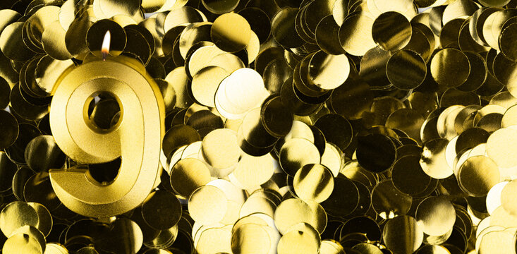 Golden number nine candle on shiny yellow confetti background. Festive backdrop for ninth birthday, anniversary or celebration. Bright greeting card with space for text.