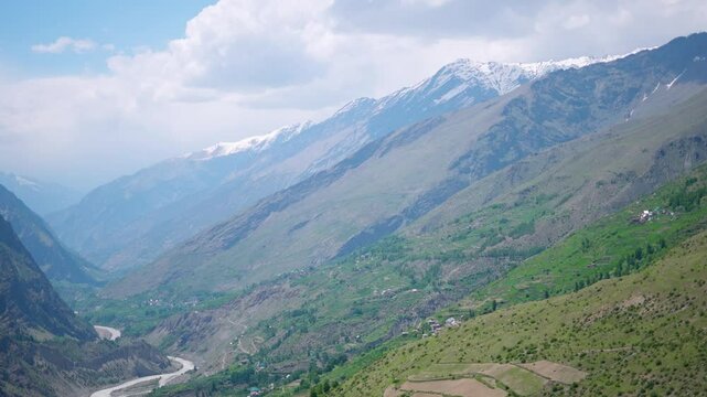 4K shot of beautiful Himalayan mountain valley with Chandrabhaga river flowing in between snowy mountain peaks with clouds above them as seen during summer season in Lahaul, Himachal Pradesh, India.