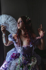 A girl dressed in the style of a Victorian boudoir, in a corset and crinoline of lilac color, in flowers
