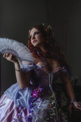 A girl dressed in the style of a Victorian boudoir, in a corset and crinoline of lilac color, in flowers