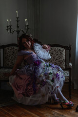 A girl dressed in the style of a Victorian boudoir, in a corset and crinoline of lilac color, in flowers