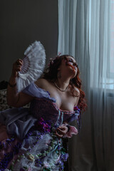 A girl dressed in the style of a Victorian boudoir, in a corset and crinoline of lilac color, in flowers
