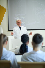 Elderly doctor explaining medical concepts to a group of students during a lecture using a digital...