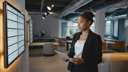 Strategic Insight: A focused businesswoman, immersed in thought, contemplates a digital display within a modern, open-plan office setting. The image highlights efficiency.