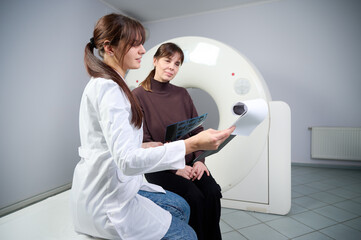Radiologist showing x-ray report to the female patient. Confident pretty doctor consulting woman in...