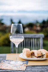 Single glass of rose wine and plate of bread on a rustic garden table at dusk with a wooden chair in the background. Dining as ritual, wholesome togetherness, mindful living, slow food