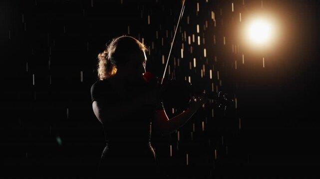 Night rain and romantic music, young woman playing violin in darkness, portrait. Silhouette of fragile tender lady holding viola and moving bow, slow motion, meditation by classical music, modern arts