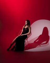 girl in black dress in studio on red background sitting on chair