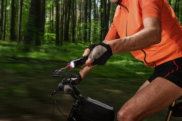 Closeup of athletic male cyclist using ultrasonic dog repeller. Stun gun with flashlight in cyclist's hand for dog repelling, ensuring safety on woodland trail.