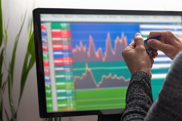 Closeup of male hands tearing credit card on the background of computer monitor with charts. Man trading stocks on monitor, back view, charts visible. Payment card destruction in progress