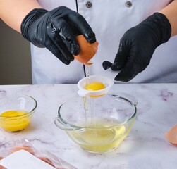 Woman in black gloves separating egg whites from yolks to make dough, dessert or meringue. Chef at...