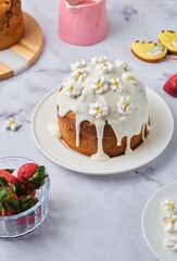 Cake filled with custard and strawberries covered with white icing and decorated with marshmello flowers on a light background. Chef at work in the kitchen. Cooking, ingredients.