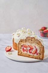 Sliced ​​cake filled with custard and strawberries covered with white icing and decorated with marshmallow flowers on a light background. Desserts strawberries.