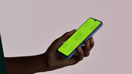 Black African-American young male using smartphone with a blank green screen. Mobile app video mockup. Vertical phone orientation
