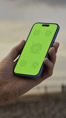 GREEN SCREEN CHROMA KEY Person holding a smartphone at a scenic beach during sunset with silhouettes of people and waves in the background