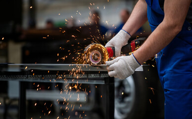 A man wearing a blue jumpsuit is using a power tool to cut metal