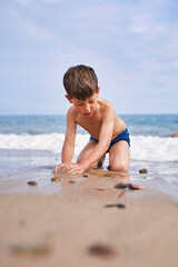 Child kneeling and molding sand on the beach