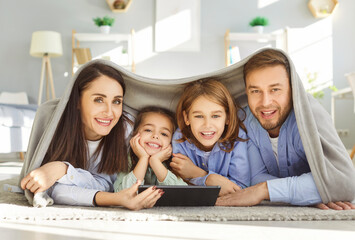 Portrait of a happy family with children enjoys online entertainment together using a tablet PC at home. Leisure, bonding, and the modern use of internet technology for fun and education.