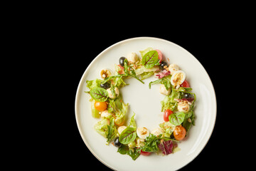Fresh salad featuring assorted greens, cherry tomatoes, olives, and nuts on a white plate against a dark backdrop