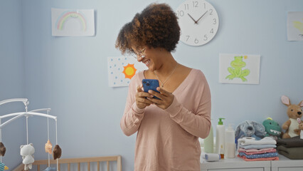 Woman smiling with phone standing in cozy bedroom with baby cradle surrounded by toys and drawings...