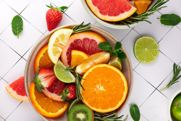 Bowl with tropical and citrus fruits: orange, lime, lemon, strawberry, kiwi, and fresh herbs on a light background. Concept of healthy eating and natural color