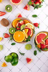 Top view of a colorful still life with fresh fruits: orange, grapefruit, lime, strawberry, kiwi, and herbs on white tiled background. Healthy style. Freshness and summer concept