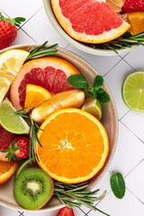 Vibrant fruit composition in bowls on a white tiled background. Orange, grapefruit, lime, lemon, strawberry, and kiwi. Bright colors and freshness. Concept of summer, freshness, and healthy lifestyle