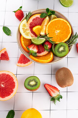 Top view of assorted fruits in a bowl: citrus slices, strawberries and kiwi with mint and rosemary. Minimalist background. Concept of healthy food and balanced diet