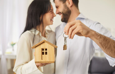 Happy family couple embraces while holding keys to new home, celebrating together new chapter of...