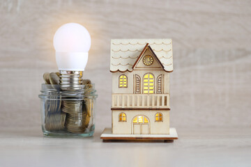 Model house and light bulb with stack of coins money in glass bottle on wooden background,Saving money and energy saving concept