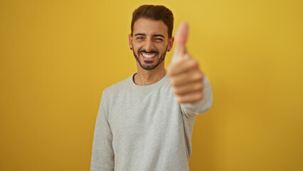 Young hispanic man smiling confidently with a thumbs-up gesture against an isolated yellow background.