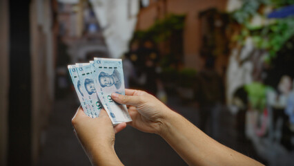 Man holding chinese yuan banknotes on street in urban setting, showcasing currency exchange in a...