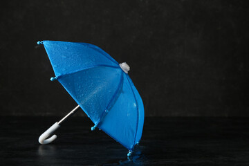 Mini blue umbrella with water drops on black background