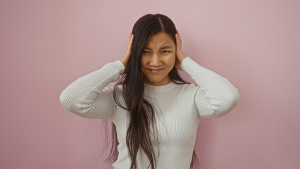 Fototapeta premium Woman holding her head with a concerned expression against a pink wall background, showcasing emotion and feminine beauty in a simple, isolated setting.
