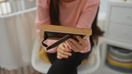 Woman sitting in baby room holding a picture frame in her hands, suggesting a personal and intimate moment in a cozy home environment, featuring a cradle and pastel decor.