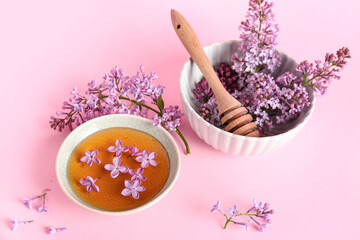 Bowl of honey with lilac twigs and flowers on pink background