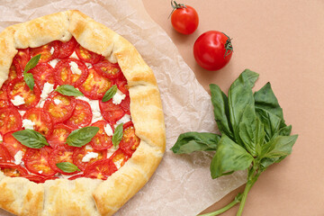 Baking paper with tasty tomato galette and basil on beige background