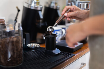 Woman barista scooping roasted coffee beans for making fresh espresso.