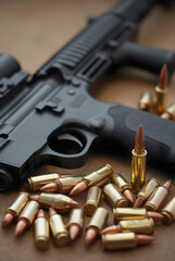 brass-cased bullets with copper-colored tips lie in front of a blurred black rifle on a wooden surface