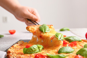 Female hand taking slice of tasty pizza margarita on white table, closeup