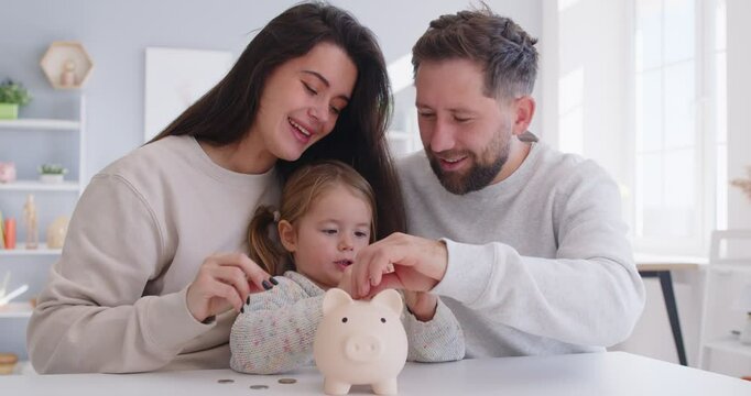 Happy young mother and father with adorable little daughter holding putting coins in pink piggy bank, caring parents and adorable girl child saving money for future, family insurance and investment