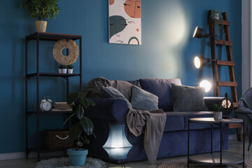 Interior of dark living room with blue sofa and glowing lamps