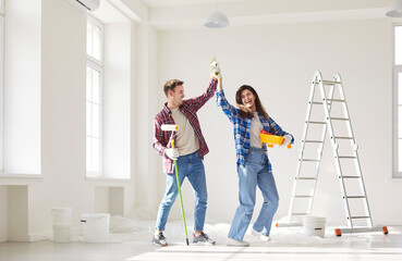Funny happy young couple having fun and dancing while painting the wall of their new apartment...